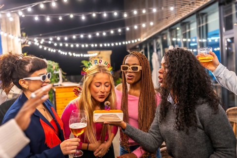 Blonde woman blowing candles of birthday cake celebrating party with friends at night in the