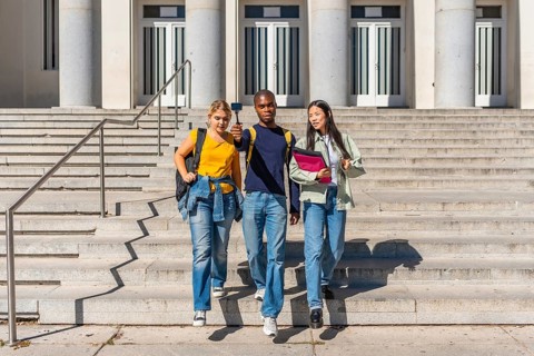 Three multi-ethnic university students walking down stairs recording online video blog with