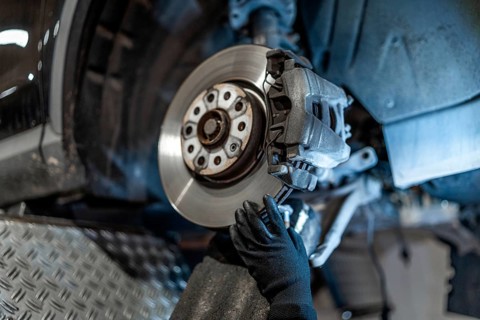 Close up of mechanic's hands wearing gloves, inspecting car brake disc and caliper during