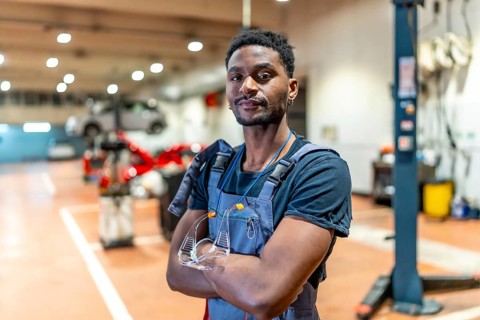 Young african american mechanic standing with crossed arms and protective eyewear in a car repair