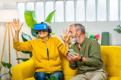 Mature couple having fun together wearing virtual reality glasses and mobile phone sitting on the