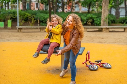 Caucasian adult mother pushing a girl on a swing in a park