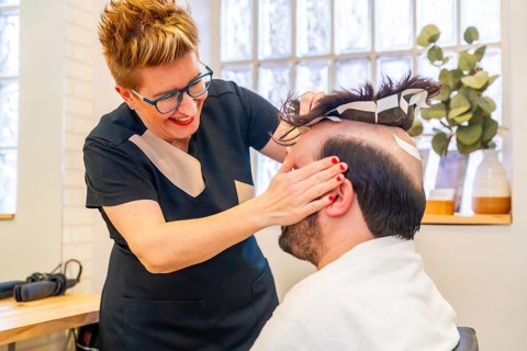 Hairdresser attaching a new capillary prosthesis to a man using adhesive stripes
