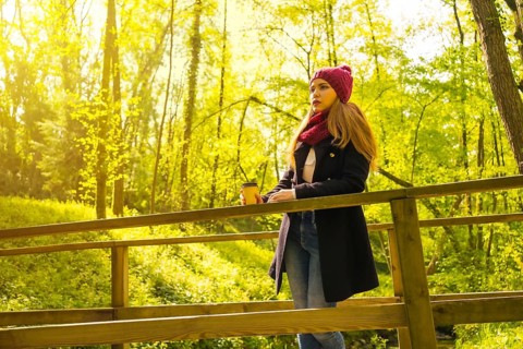 Young man with a black jacket, scarf and red woolen hat enjoying in an autumn park