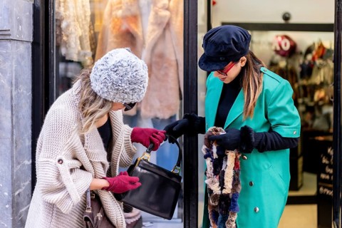 Young blonde girl shopping in the city and served by a shop assistant, looking at shop windows of