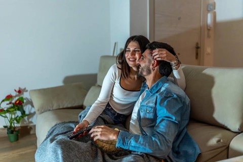Young loving couple watching television, eating popcorn and relaxing on sofa at night at home