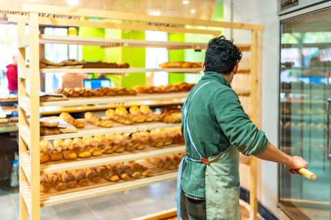 Rear view of a latin young man placing baked bread to shop using a peel