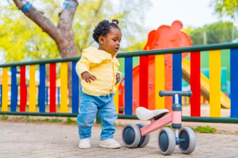 Full length photo of an african baby girl in a playground with a toy bike alone