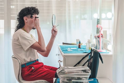 Young make-up artist applying eyebrow pencil while looking in a mirror and getting ready for a