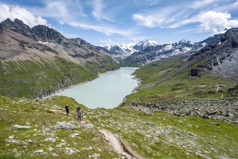 Two mountaineers on a hiking trail, view of a blue mountain lake, Lac des Dix reservoir, mountain
