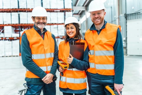 Warehouse workers wearing safety vests and hard hats smiling in a logistics center, managing
