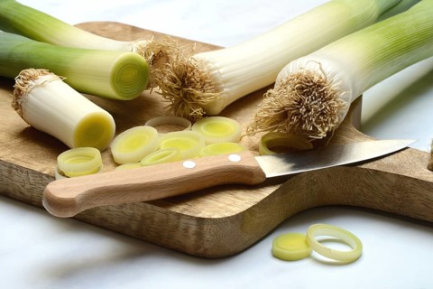 Leek, leek sticks and leek rings on a chopping board with a knife