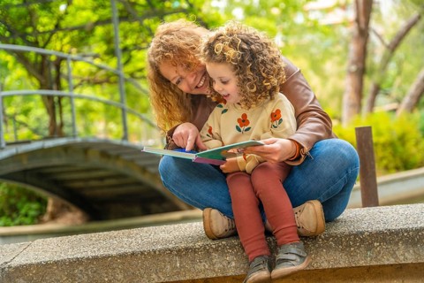 Girl sitting on the lap of her mother reading a book in a park