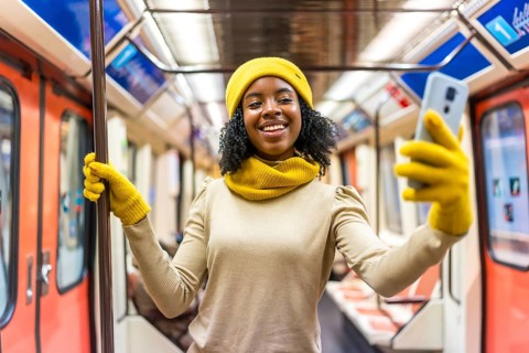 Smiling young woman wearing yellow winter accessories takes a selfie with smartphone while