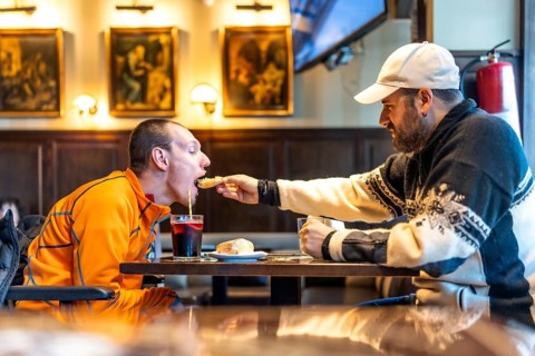 Heartwarming moment of friendship as a man helps his disabled friend enjoy a meal at a restaurant,