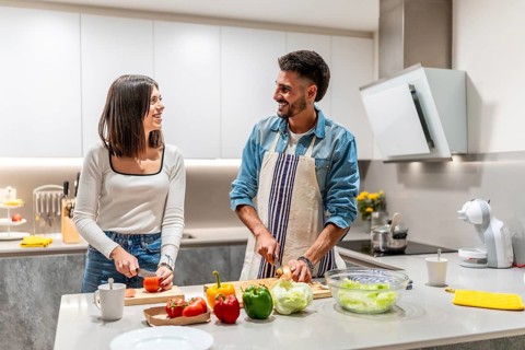 Young smiling couple preparing a healthy salad together in their modern kitchen, enjoying their