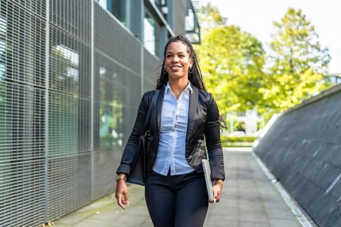 Real estate agent latin woman walking outside building holding laptop