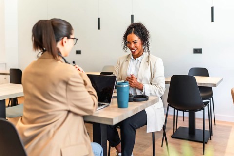Two businesswomen are working together on a project in a modern office space, using a laptop and