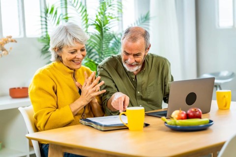 Senior couple going over their finances while sitting on their living room expressing happiness