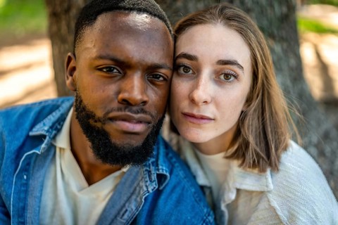 Close-up frontal view of a multiracial couple together cheek to cheek in a park