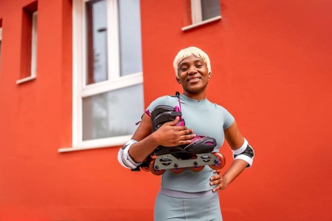 Portrait of african female skater with inline skates on shoulder standing outdoors next to red