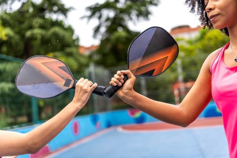 Cropped close-up photo of multiracial women clashing pickelball rackets before playing together