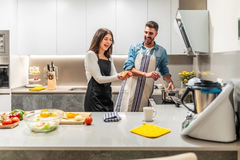Cheerful couple wearing aprons preparing healthy meal together, having fun in contemporary kitchen