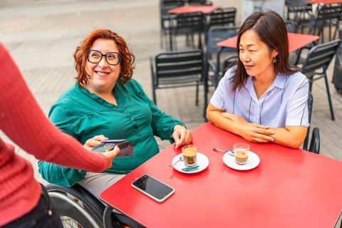 Woman with disability and asian friend paying with credit card in a sidewalk cafeteria