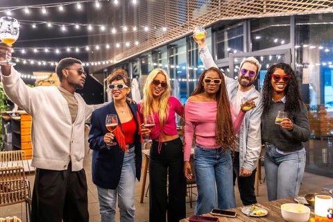 Multi-ethnic friends raising glasses celebrating party at night in the terrace of a modern bar
