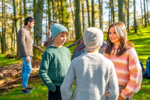Caucasian sister and brothers talking standing in a green forest while camping with their parents
