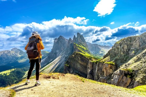 Female tourist with backpack admiring the odle mountain range in the italian dolomites on a sunny