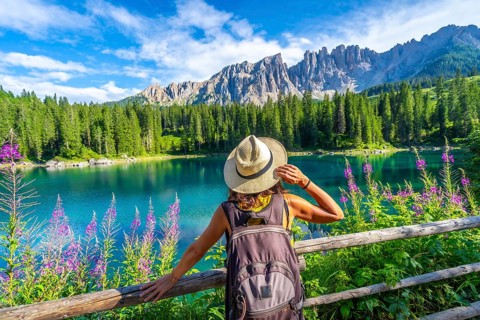 Female tourist admiring the stunning turquoise waters of lake carezza with latemar mountain range