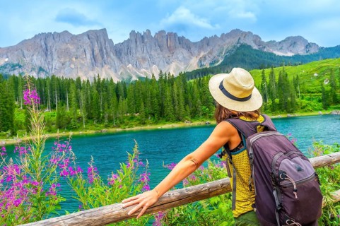 Female hiker with backpack enjoying the stunning turquoise waters of lake carezza with the latemar