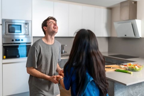 Asian woman and caucasian man sharing a joyful moment in a bright, contemporary kitchen,