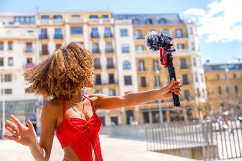 Female latin young vlogger recording a video in the city using mobile phone and microphone