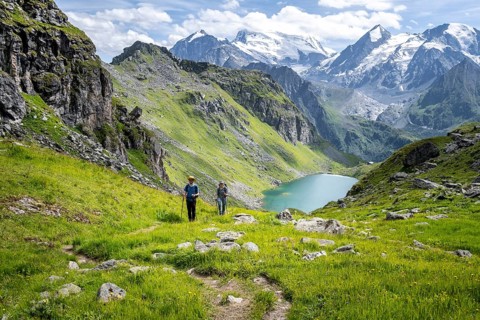 Hiker and mountain lake Lac de Louvie with glaciated summit of the Grand Combin, Val de Bagnes,