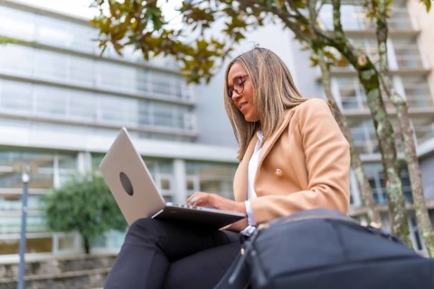 Side view low angle of a latin confident businesswoman using laptop sitting in city bench