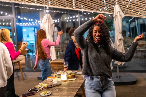 Latin woman dancing happily while partying with diverse friends in a roof bar at night