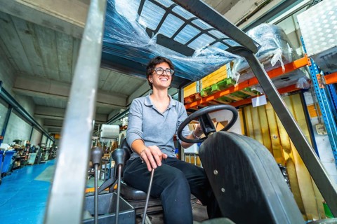 Happy female manual worker using forklift in a warehouse of a cnc metallurgic factory