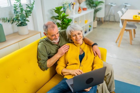 Elevated view photo of a casual senior couple lying on the sofa relaxed using laptop