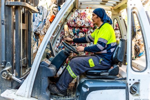 Side view full length photo of a latin man worker moving plastic bales driving forklift in a