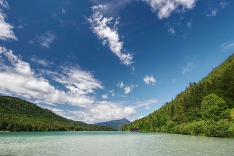 A green lake surrounded by densely wooded hills under a cloudy sky, Walchensee, Jachenau, Bavaria,
