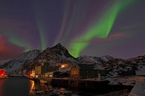 Night scene with northern lights in the sky, snow-covered mountains and houses by the water,