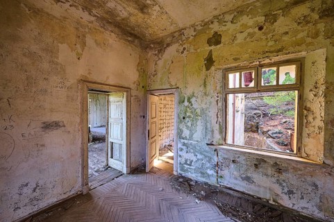 Dilapidated room with dirty walls, an open window and open door, showing green mould and