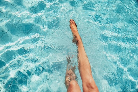 Beautiful legs of a woman splashing in a turquoise-coloured pool