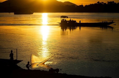 Fishermen fishing next to boats in the Brahmaputra river, during sunset in Guwahati, Assam, India