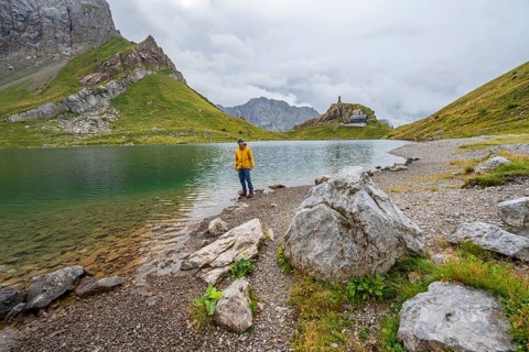 Mountaineer in yellow jacket at the mountain lake, view over the Wolayersee lake to the alpine club