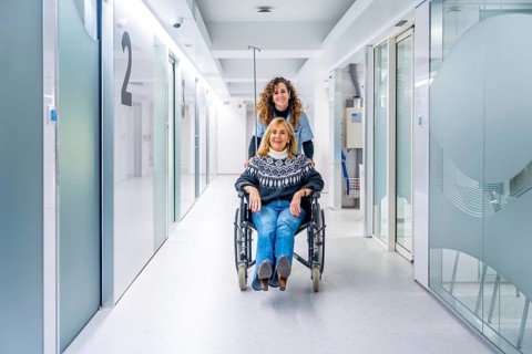 Nurse carrying a mature woman in wheelchair along the hospital corridor