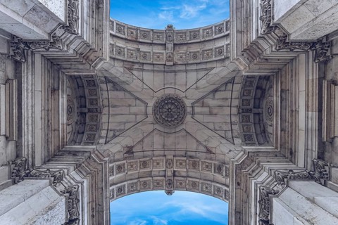View of ornate stone arch pattern with symmetrical details and clear blue sky in the background,