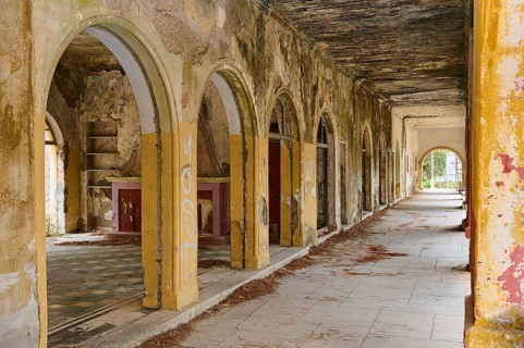 A dilapidated hall with arches and dirty walls, showing signs of neglect and wall decay, Italian